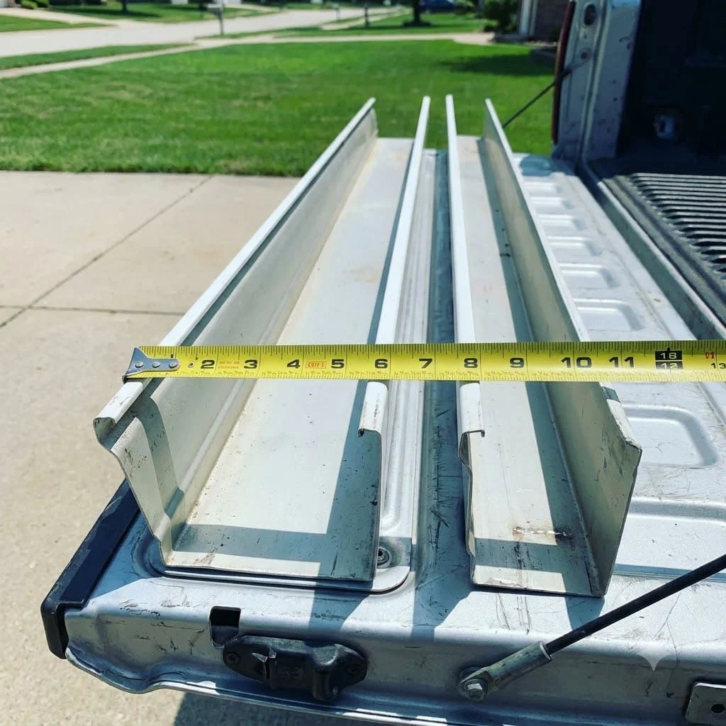 A five-inch and a six-inch K-style gutter section side by side on a truck tailgate with a tape measure across the wider trough