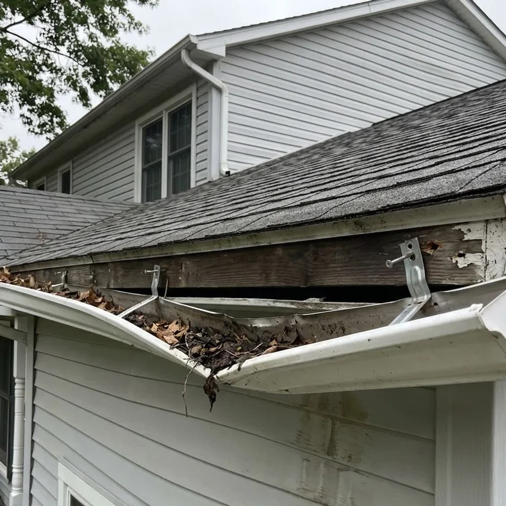 White aluminum gutter sagging and pulled away from a weathered fascia board, with loose hangers exposed, on a vinyl-sided house